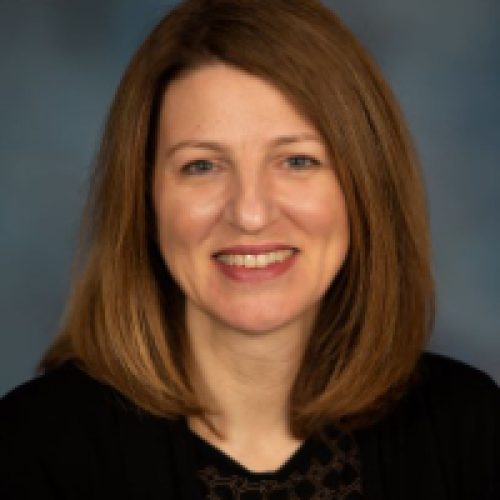 Professional headshot of a smiling woman against a neutral background.